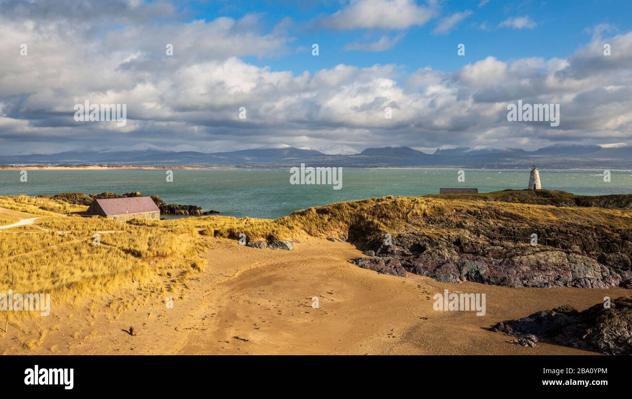 Une vue sur Twr Bach, la maison du canot de sauvetage et les montagnes enneigées de Snowdonia depuis l'île de Llanddwyn, Anglesey Banque D'Images