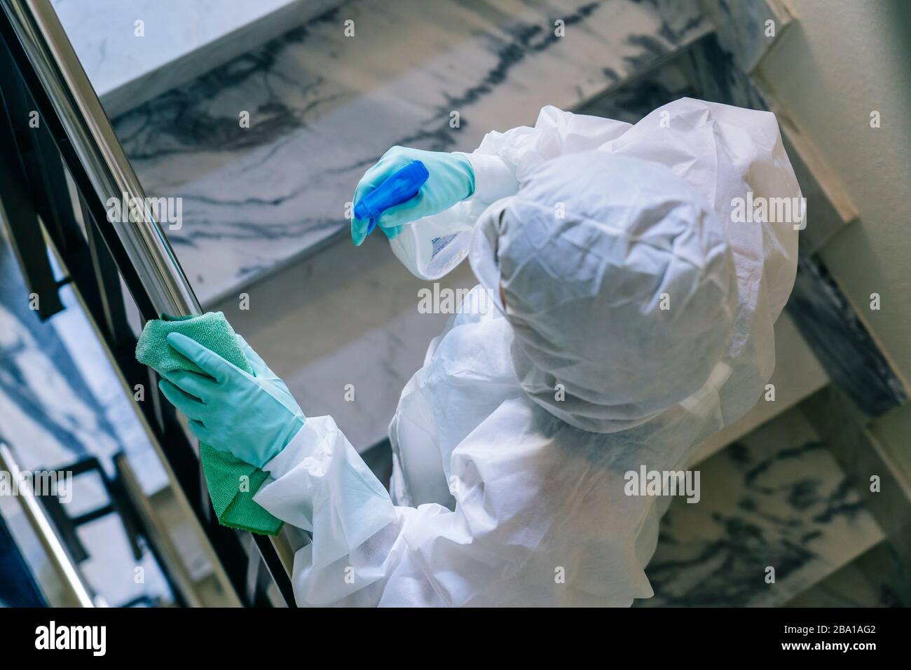 Une personne portant un masque, des gants et une combinaison de sécurité nettoie et désinfecte une porte d'une communauté plate face à une pandémie de virus, protégée et protégée Banque D'Images