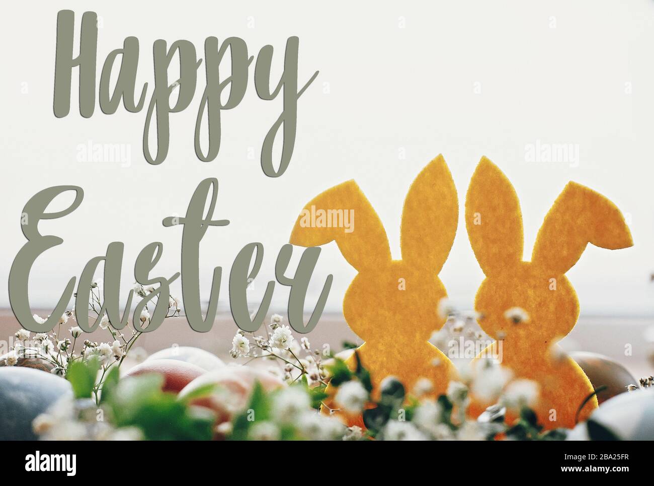 Texte de joyeuses Pâques. Carte de voeux de Pâques. Des œufs de pâques élégants, un lapin jaune au nid de fleurs printanières sur une table rustique. Œufs de pâques teints naturels et r Banque D'Images