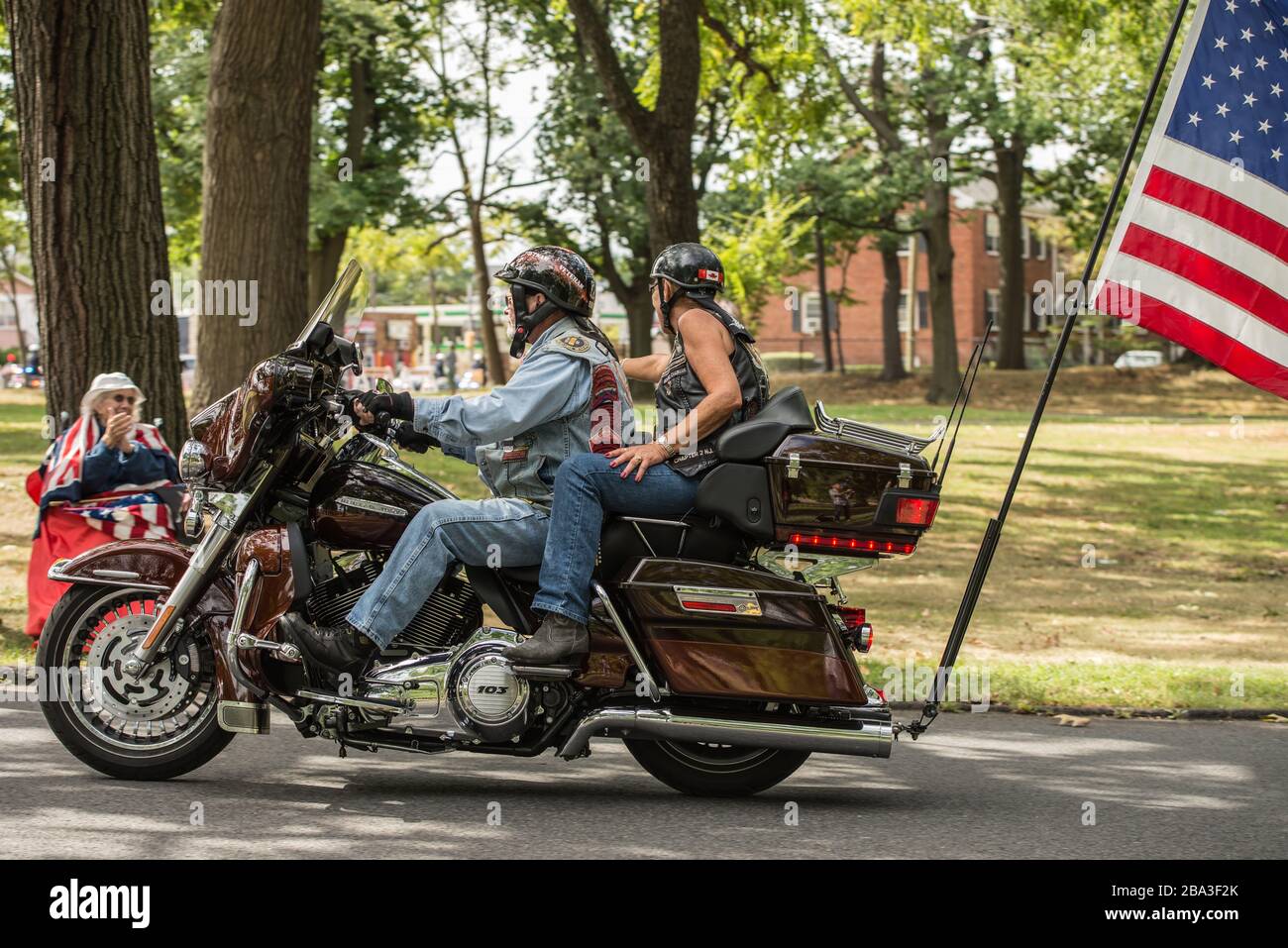 Rouler les membres du tonnerre sur une moto avec un grand drapeau attaché, lors d'un rassemblement des anciens combattants du Vietnam. Une mère Gold Star est assise en arrière-plan. Banque D'Images