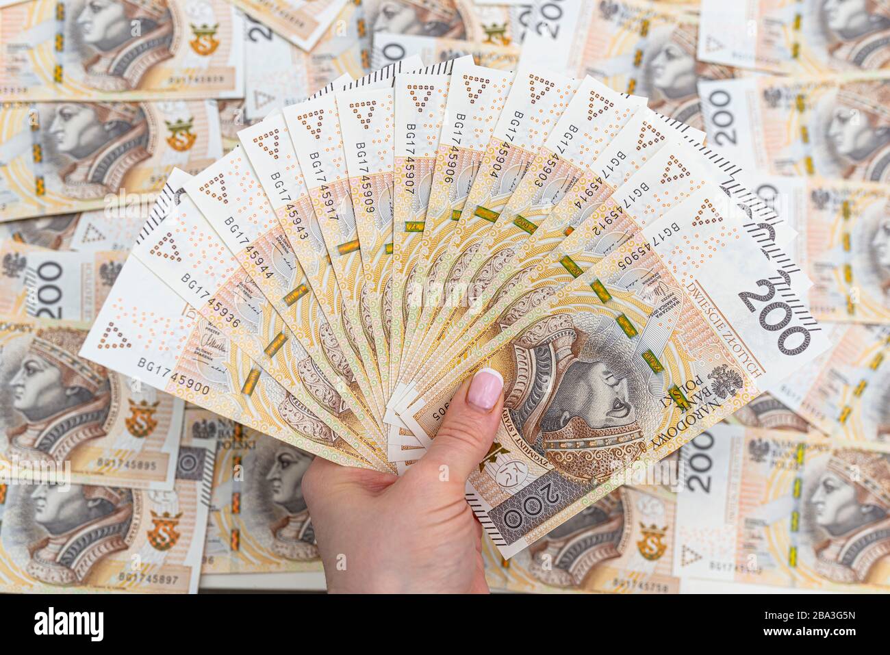 La femme tient les billets polonais sur le devant, valeur faciale 200 PLN disposés en éventail, en arrière-plan une pile de billets polonais. Banque D'Images