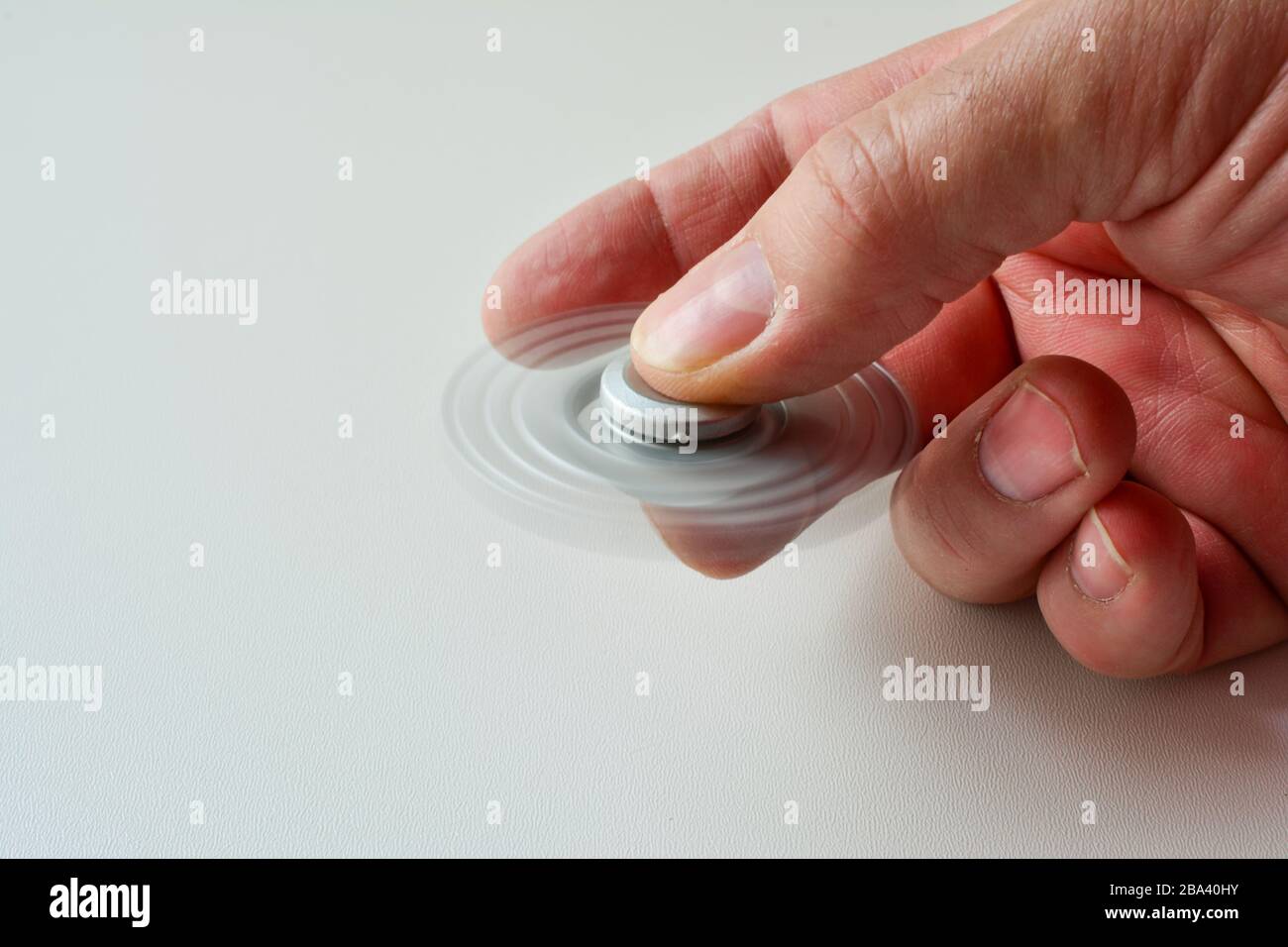 Disque de fidget couleur argent en mouvement dans la main de l'homme sur fond blanc, vue latérale, espace de copie sur la gauche Banque D'Images