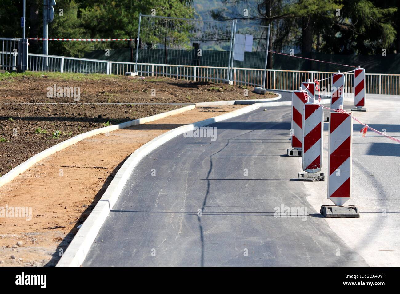 Route fraîchement pavée encore en construction remplie de panneaux d'avertissement rouges et blancs dépouillés entourés d'un nouveau bord de béton et non fini Banque D'Images