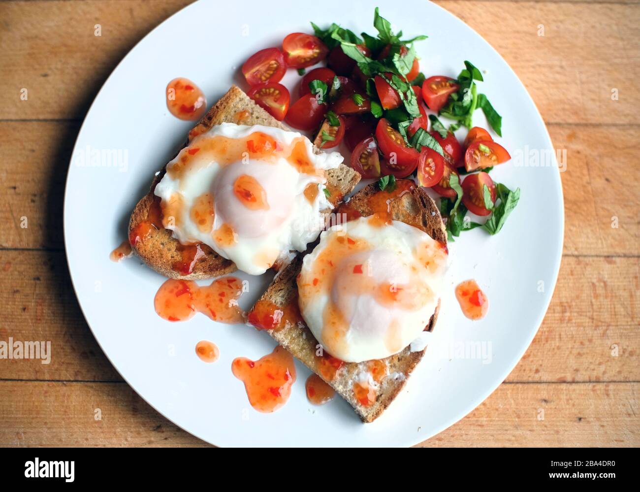 Œufs pochés sur pain grillé avec tomates, basilic et sauce au piment doux. Banque D'Images