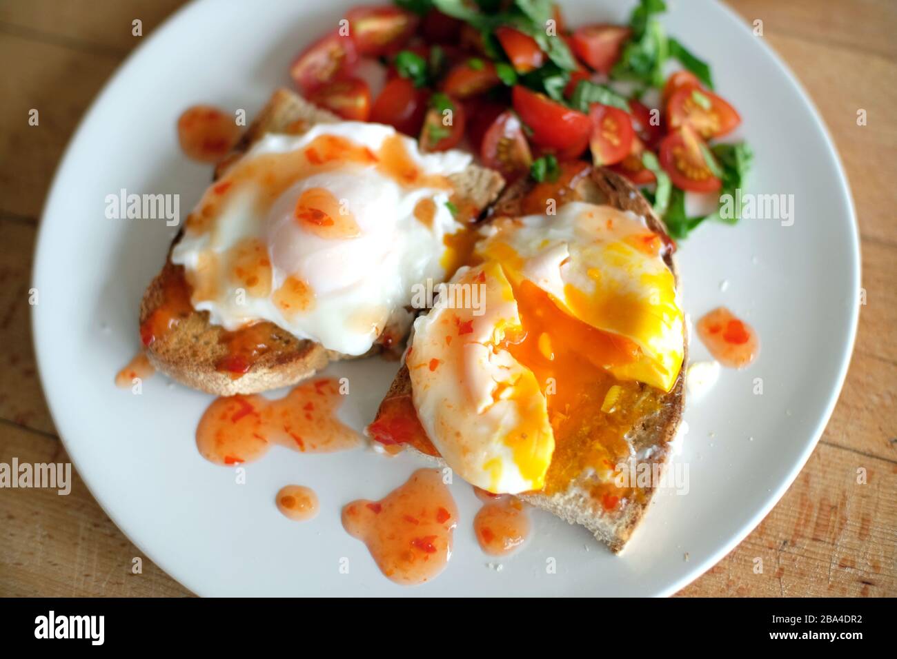 Œufs pochés sur pain grillé avec tomates, basilic et sauce au piment doux. Banque D'Images