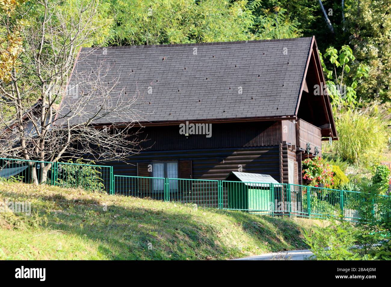 Vue latérale de la petite cabane en bois brun foncé de montagne récemment construite entourée d'une clôture en métal vert et d'une végétation dense Banque D'Images