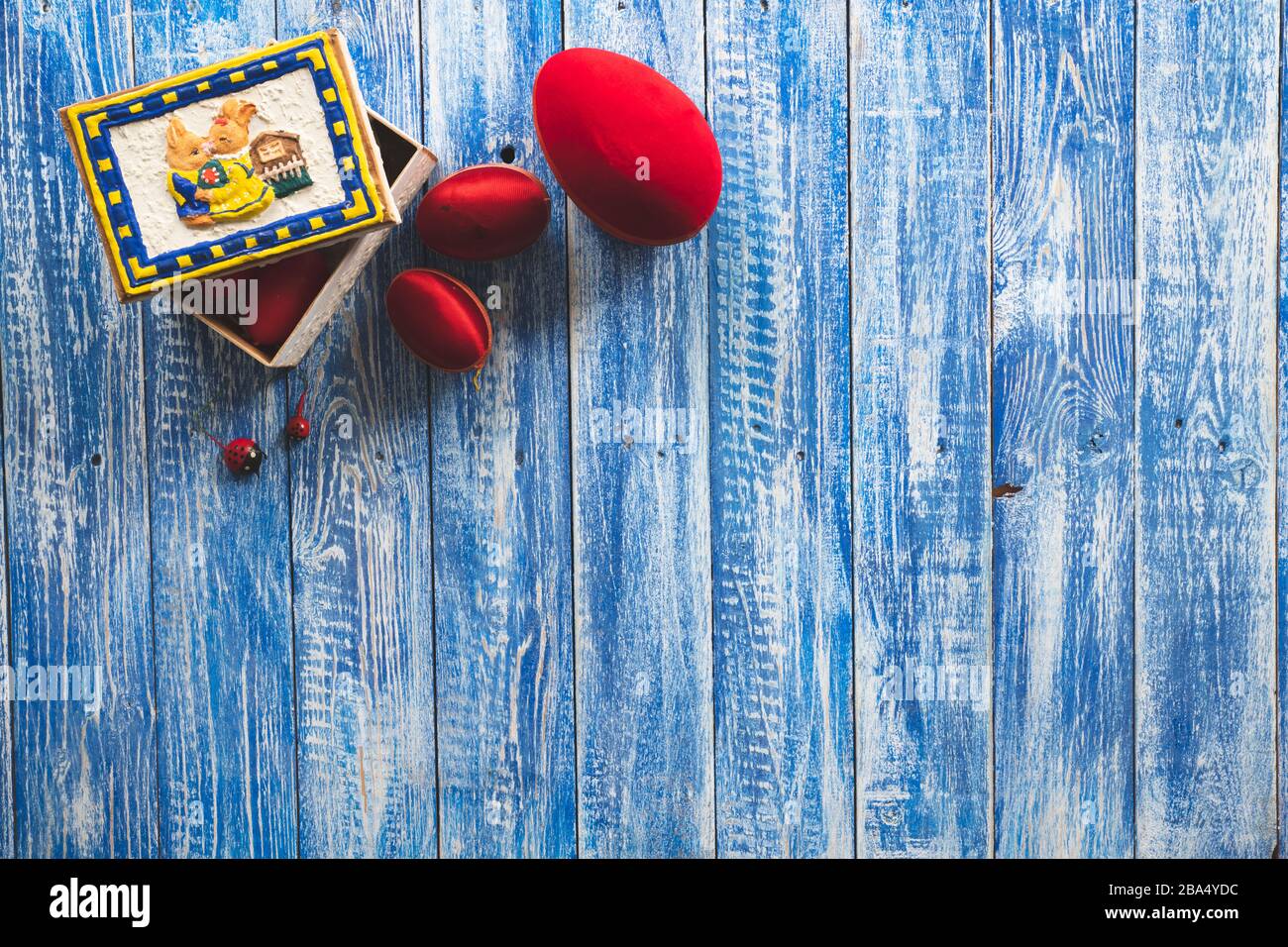 Fond de Pâques sur une surface en bois bleu clair avec des œufs décoratifs rouges et une boîte de lapin Banque D'Images