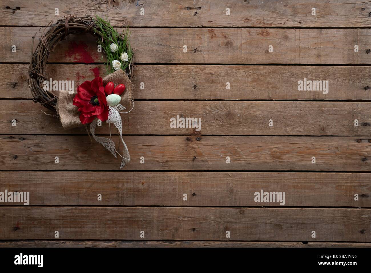 Couronne décorative de Pâques avec une fleur rouge et des œufs blancs et rouges peints sur une vieille table rustique en bois Banque D'Images