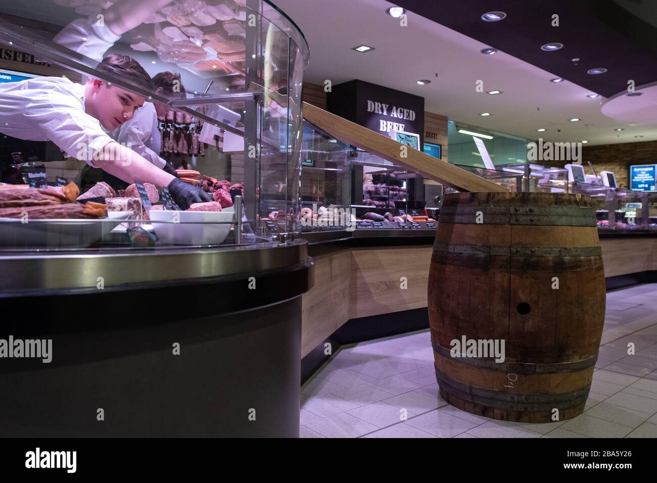 Duderstadt, Allemagne. 25 mars 2020. Marvin Gatzemeier, un employé d'un marché d'Edeka, se tient derrière un comptoir de viande où une « lame de colis » auto-fabriquée a été installée. Avec l'aide de la lame auto-construite, le contact direct lors de la remise des saucisses emballées doit être évité. La vie publique en Basse-Saxe est fortement affectée par des mesures visant à contenir le coronavirus. Crédit: Swen Pförtner/dpa/Alay Live News Banque D'Images