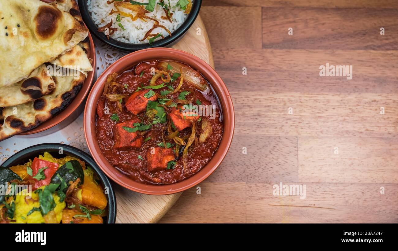 Sélection de curry de tapas de style indien à base de poulet, d'agneau, de légumes, d'ailes de poulet tandoori et de pain naan et de chips Banque D'Images