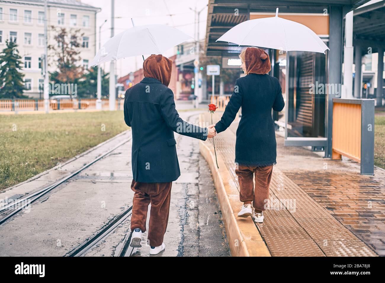 un jeune couple marche le long de la route sous la pluie. homme et femme sous parapluie en costume d'ours Banque D'Images