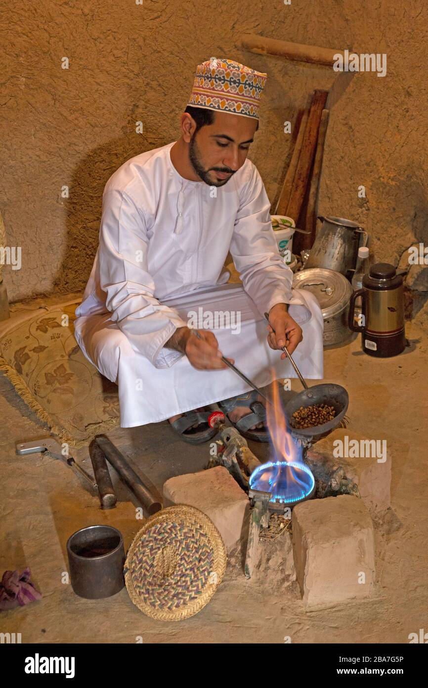 Un homme omanais dans une robe traditionnelle omanaise, torréfaction des grains de café de la manière traditionnelle. Banque D'Images