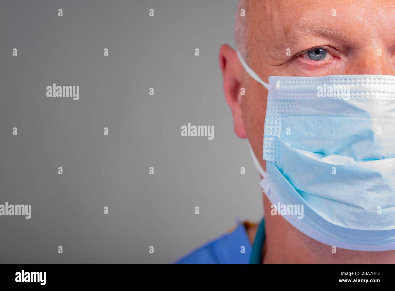 Gros plan, portrait d'un médecin d'hôpital caucasien en gommages bleus, regardant le spectateur et portant un masque chirurgical, contre un backgrou gris Banque D'Images