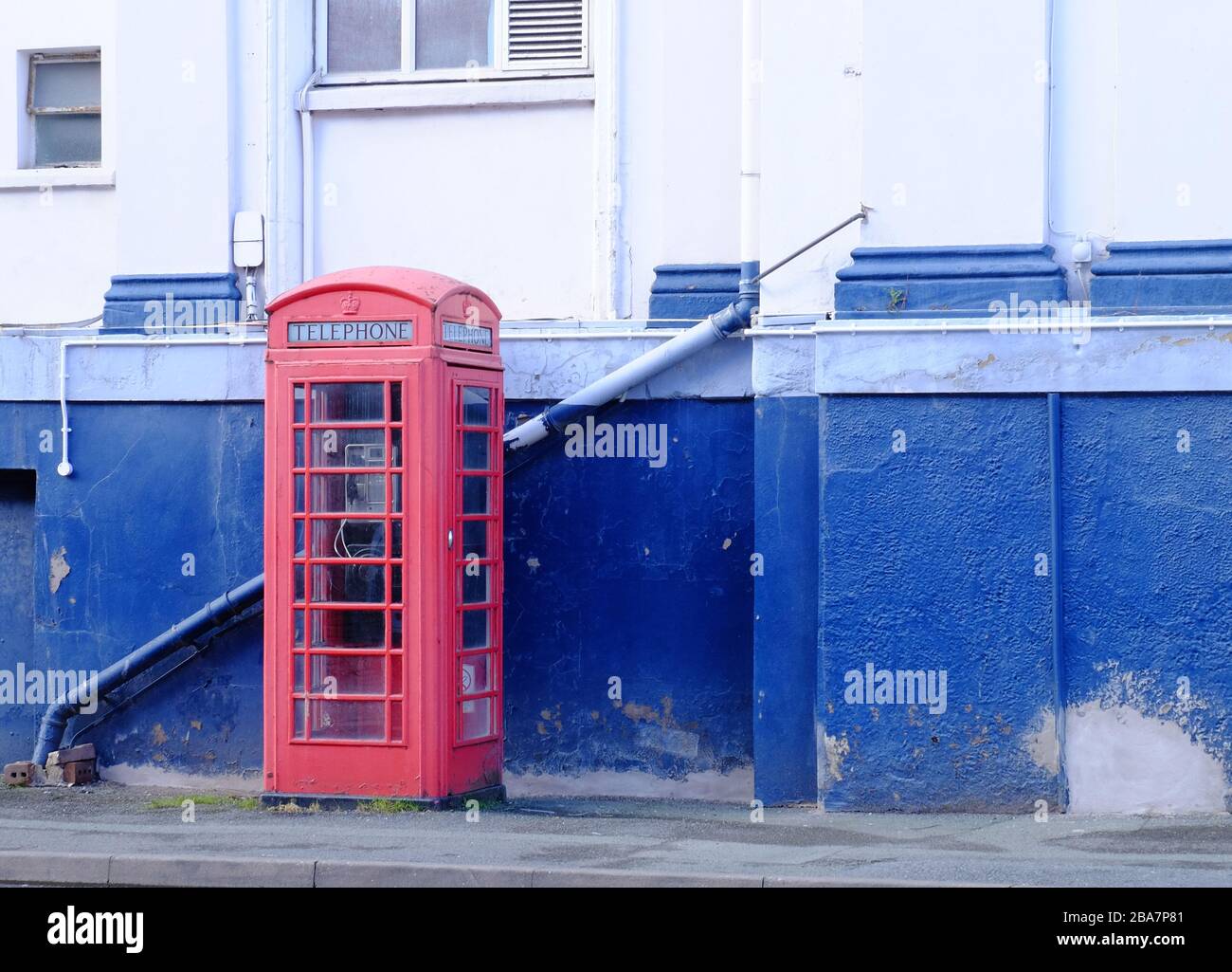 Ancienne boîte d'appel téléphonique rouge contre un mur bleu et blanc, Royaume-Uni Banque D'Images