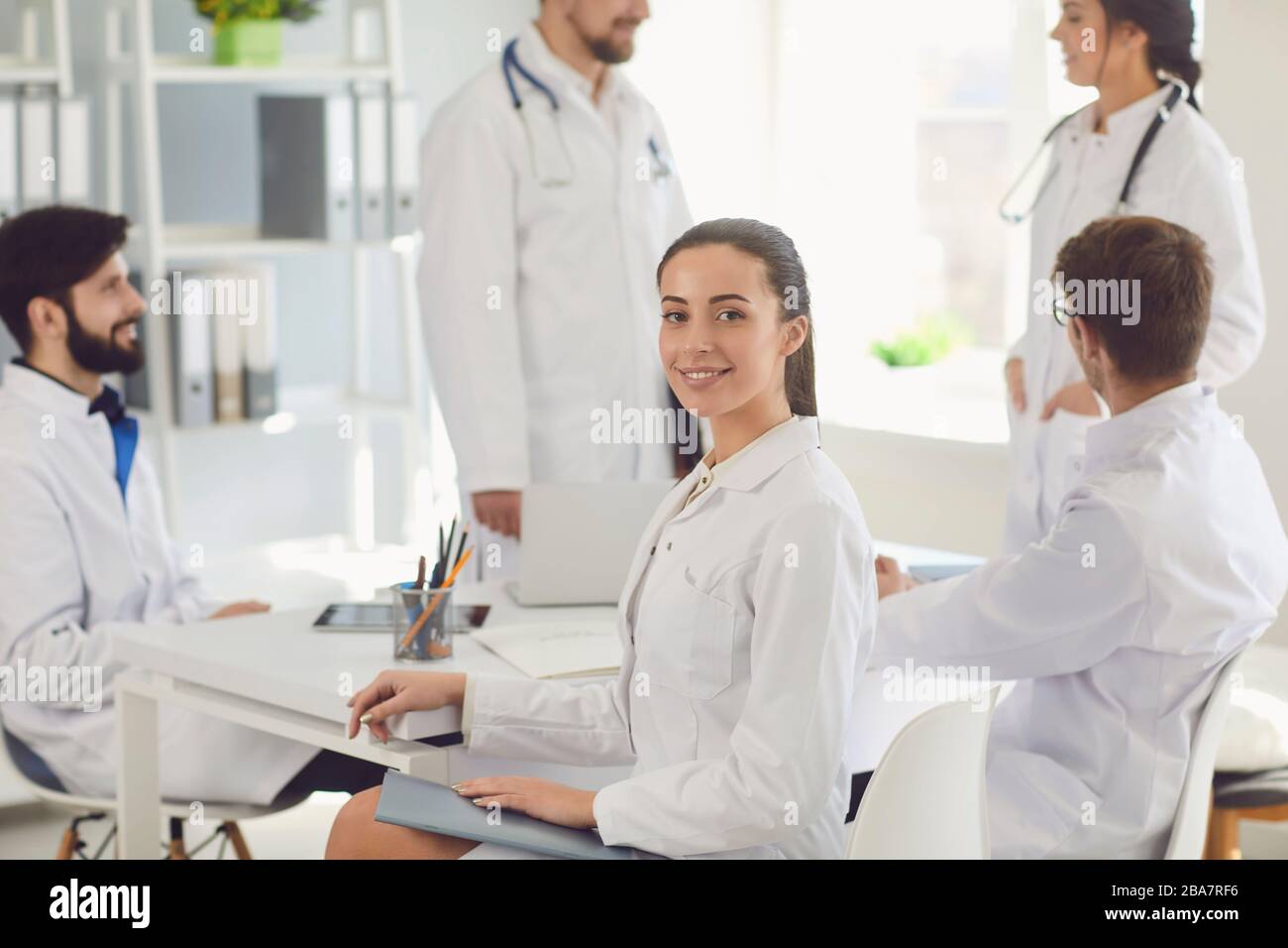 Une femme médecin assise à une table avec des collègues dans des blouses de laboratoire blanches à un hôpital médical. Banque D'Images