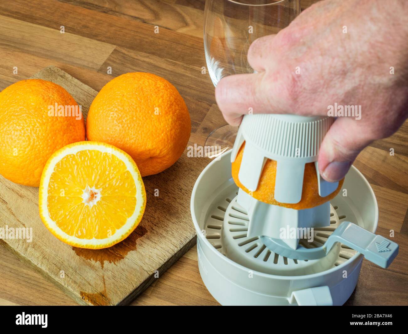 Oranges et demi-orange sur une planche à découper et une main en pressant une orange avec un presse-fruits orange sur un plan de travail de cuisine en bloc de bois Banque D'Images