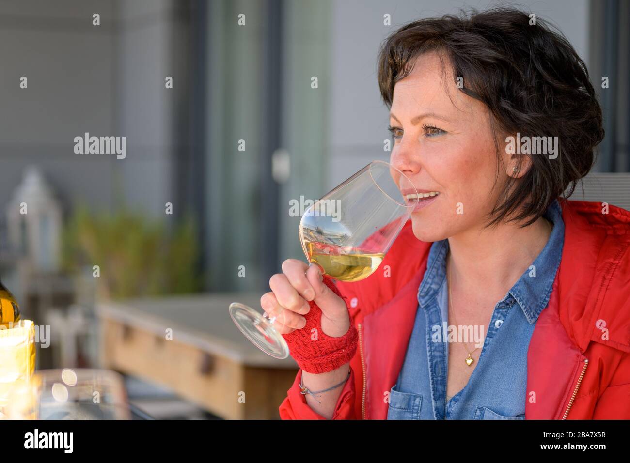 Une femme à la mode sirotant un verre de vin blanc lorsqu'elle est assise à une table de restaurant en plein air dans une vue de profil avec une expression réfléchie Banque D'Images