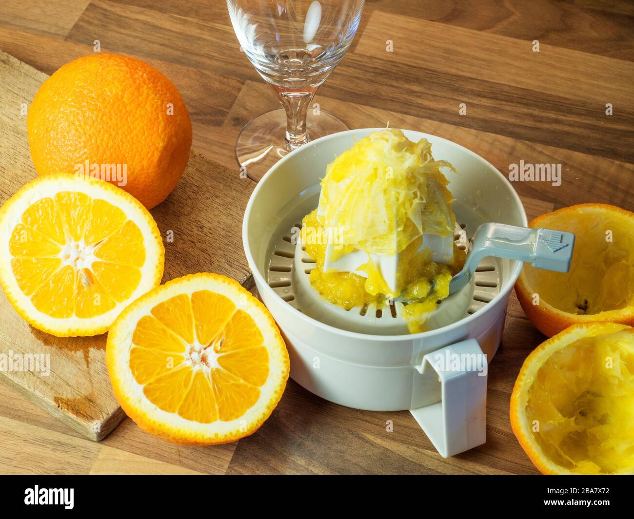 Oranges et demi-oranges sur une planche à découper avec un presse-fruits orange et des oranges fraîchement pressées sur un plan de travail de cuisine en bloc de bois Banque D'Images