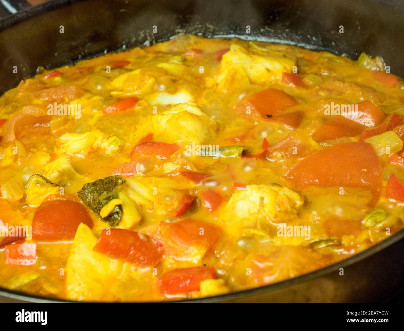 Curry composé de poivrons rouges de poisson blanc et de tomates qui se simmeraient dans une poêle sur une table de cuisson Banque D'Images