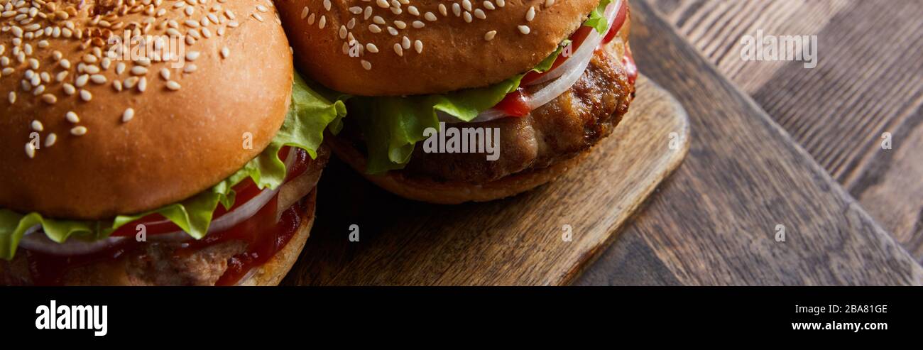 photo panoramique à angle élevé de hamburgers sur planche à découper en bois, couverts, huile, vinaigre et bouteilles de bière Banque D'Images
