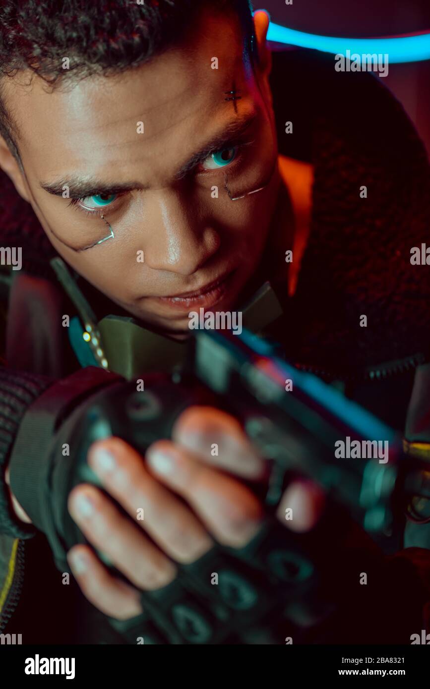 focalisation sélective du joueur de cyberpunk biracial armé avec des plaques métalliques sur le pistolet de maintien du visage Banque D'Images