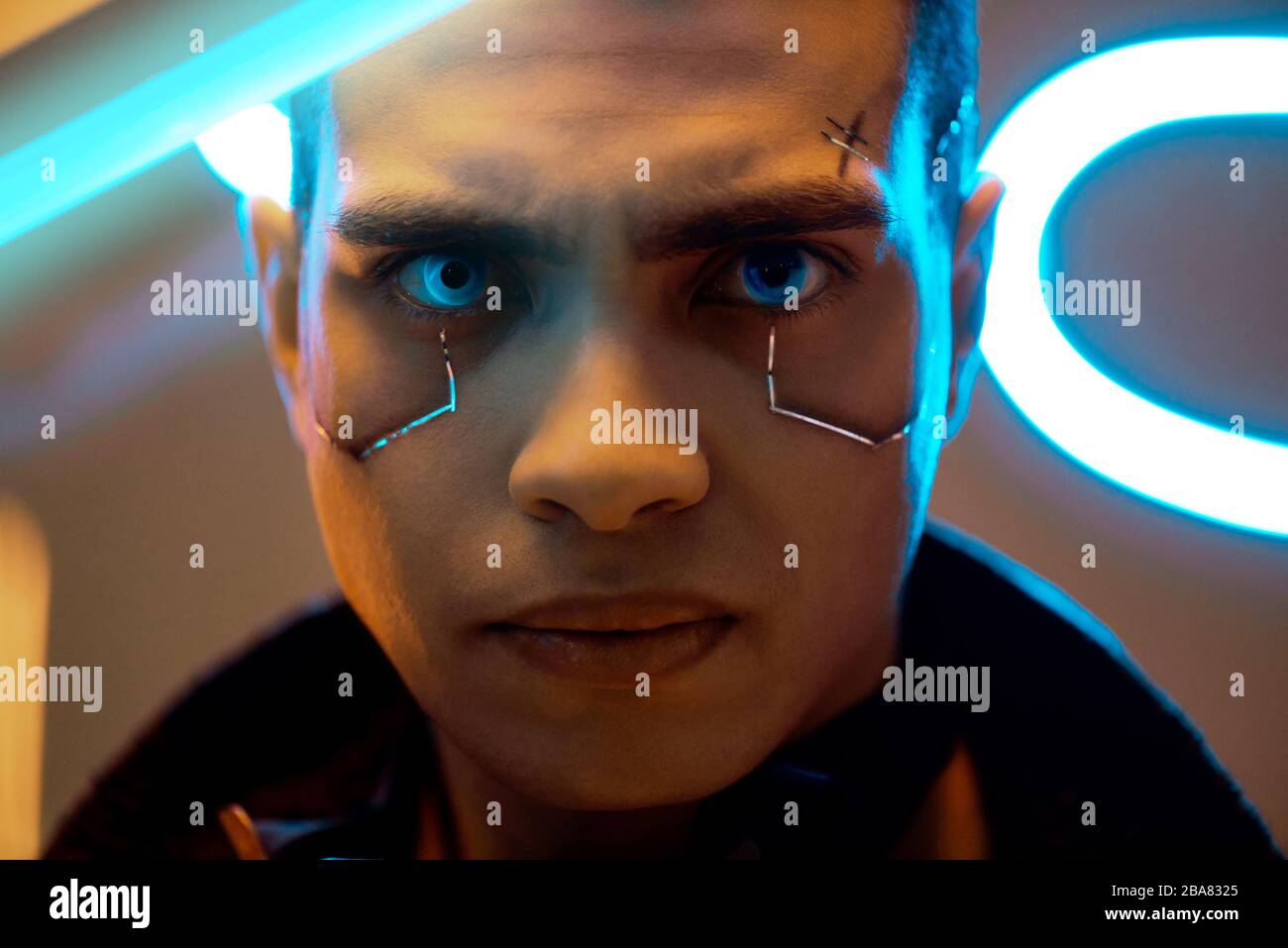 lecteur de cyberpunk biracial avec plaques métalliques sur le visage regardant l'appareil photo près de l'éclairage au néon Banque D'Images