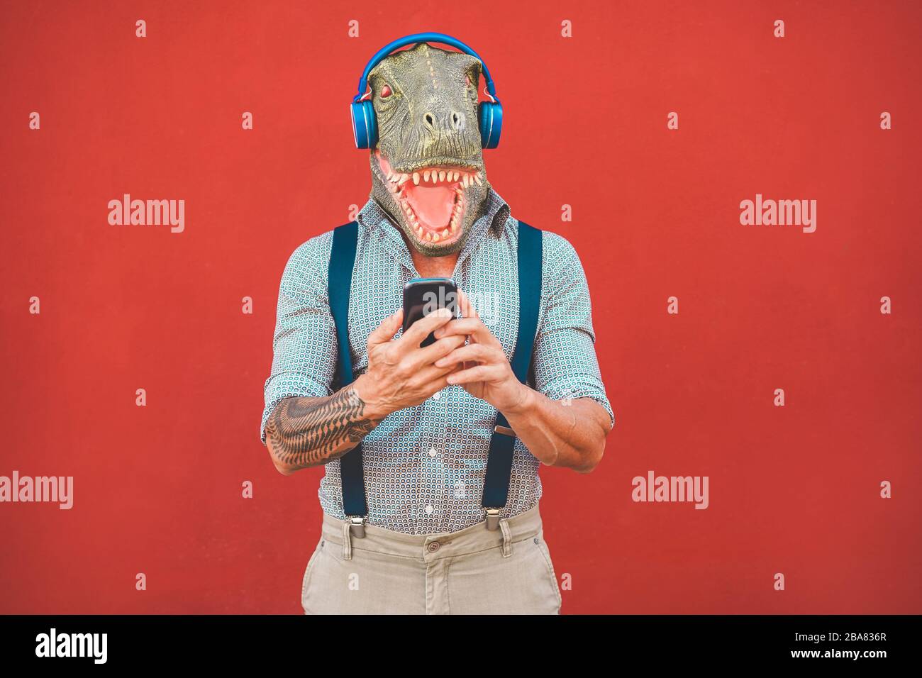 Homme tatoué avec masque t-rex utilisant un smartphone tout en écoutant de la musique - Crazy senior gars choisir la liste de lecture de l'application de téléphone mobile - tendances technologiques et Banque D'Images