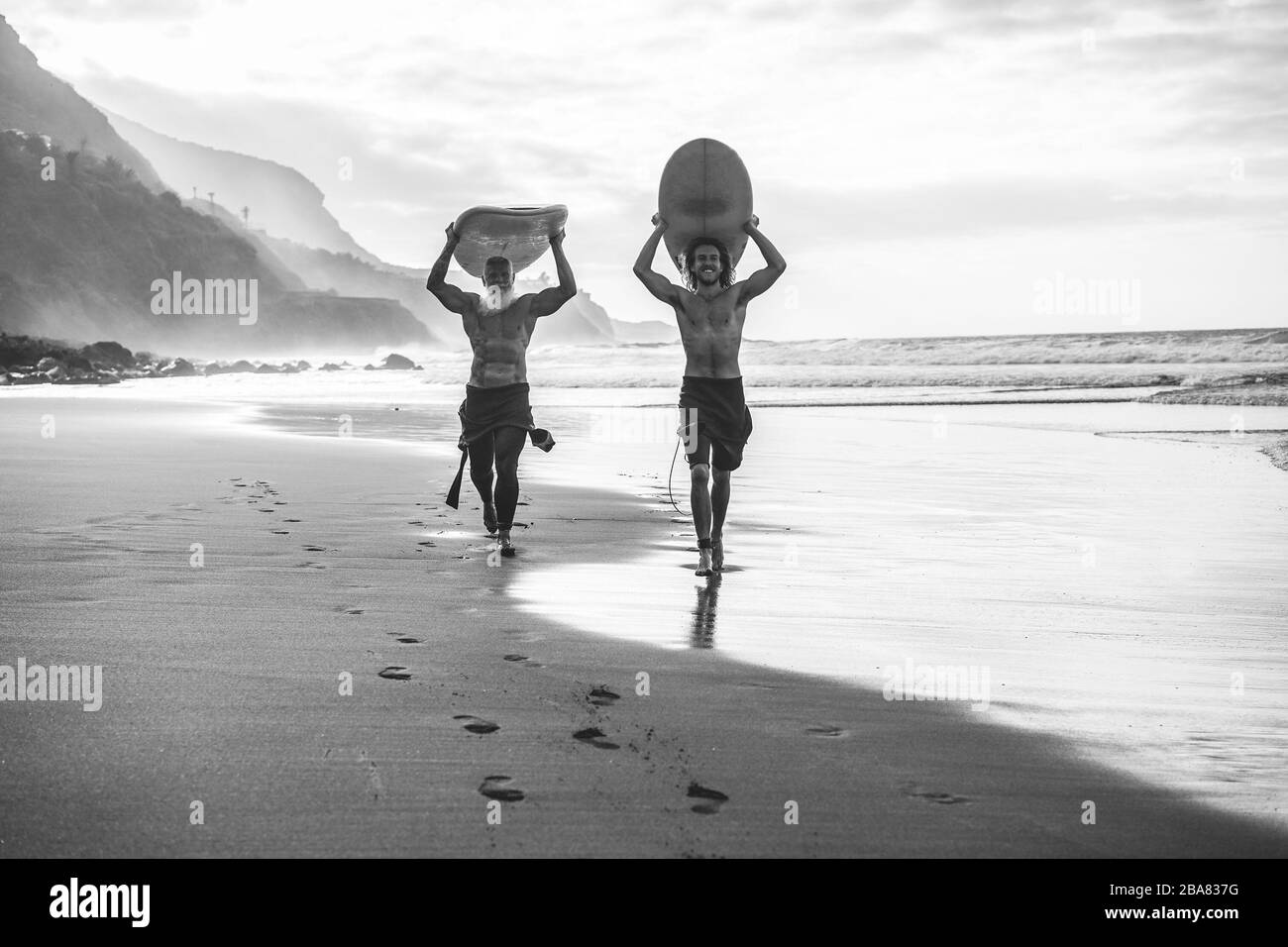 Des amis de plusieurs générations qui vont surfer sur la plage tropicale - des familles qui s'amusent à faire du sport extrême - l'accent principal sur le visage des jeunes - Noir et blanc Banque D'Images