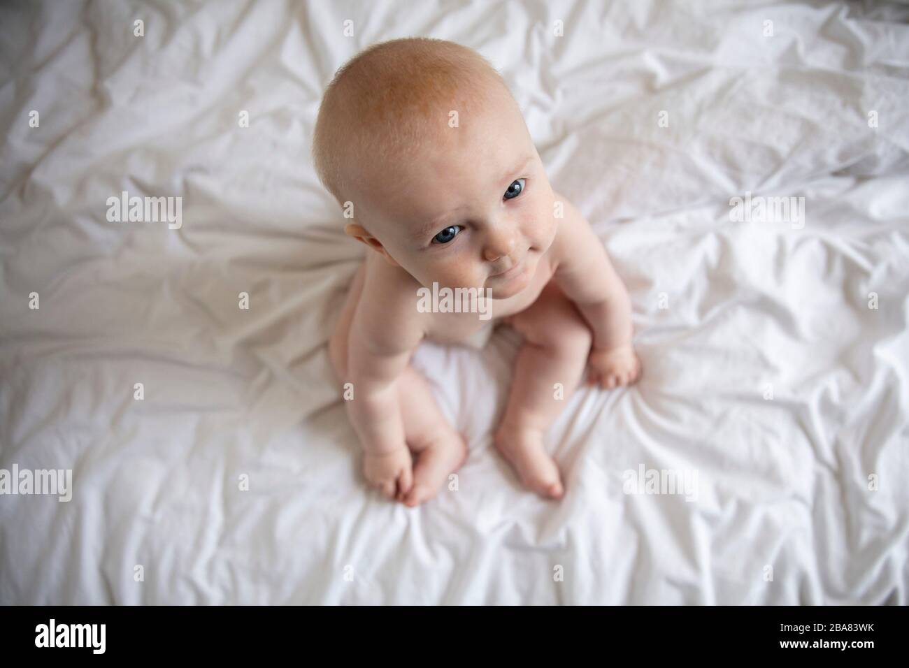 Adorable bébé de 6 mois assis sur un lit regardant l'appareil photo Banque D'Images