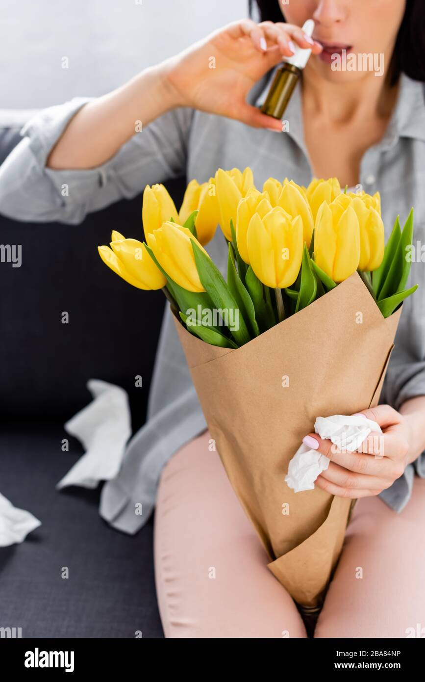 vue réduite d'une femme souffrant d'allergie au pollen, assise sur un canapé avec fleurs et contenant un spray nasal Banque D'Images