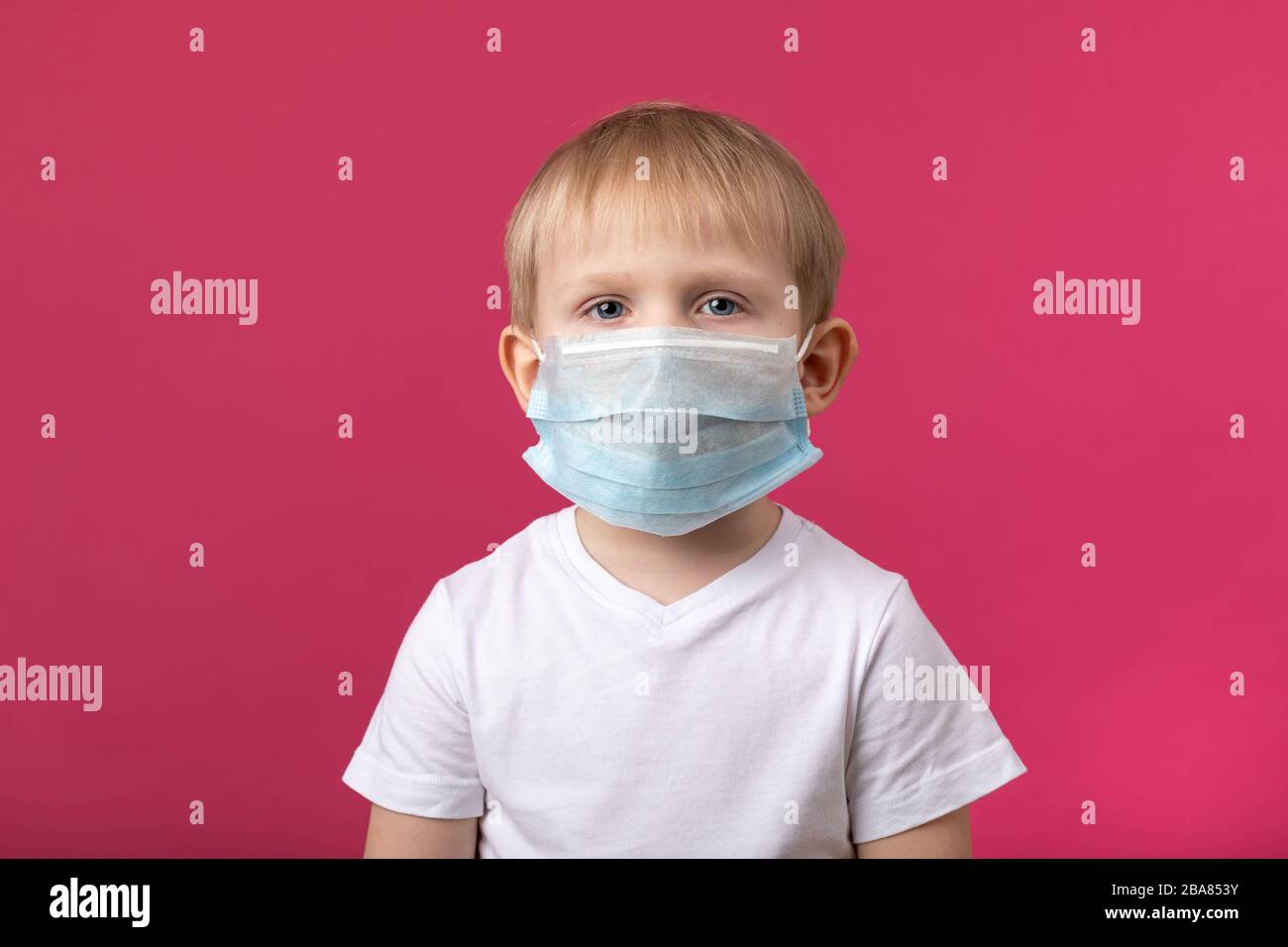 Enfant preschooler garçon closeup tourné dans le masque médical regardant la caméra sur un fond rose. Pour les articles du coronavirus, la quarantaine et la protectio Banque D'Images