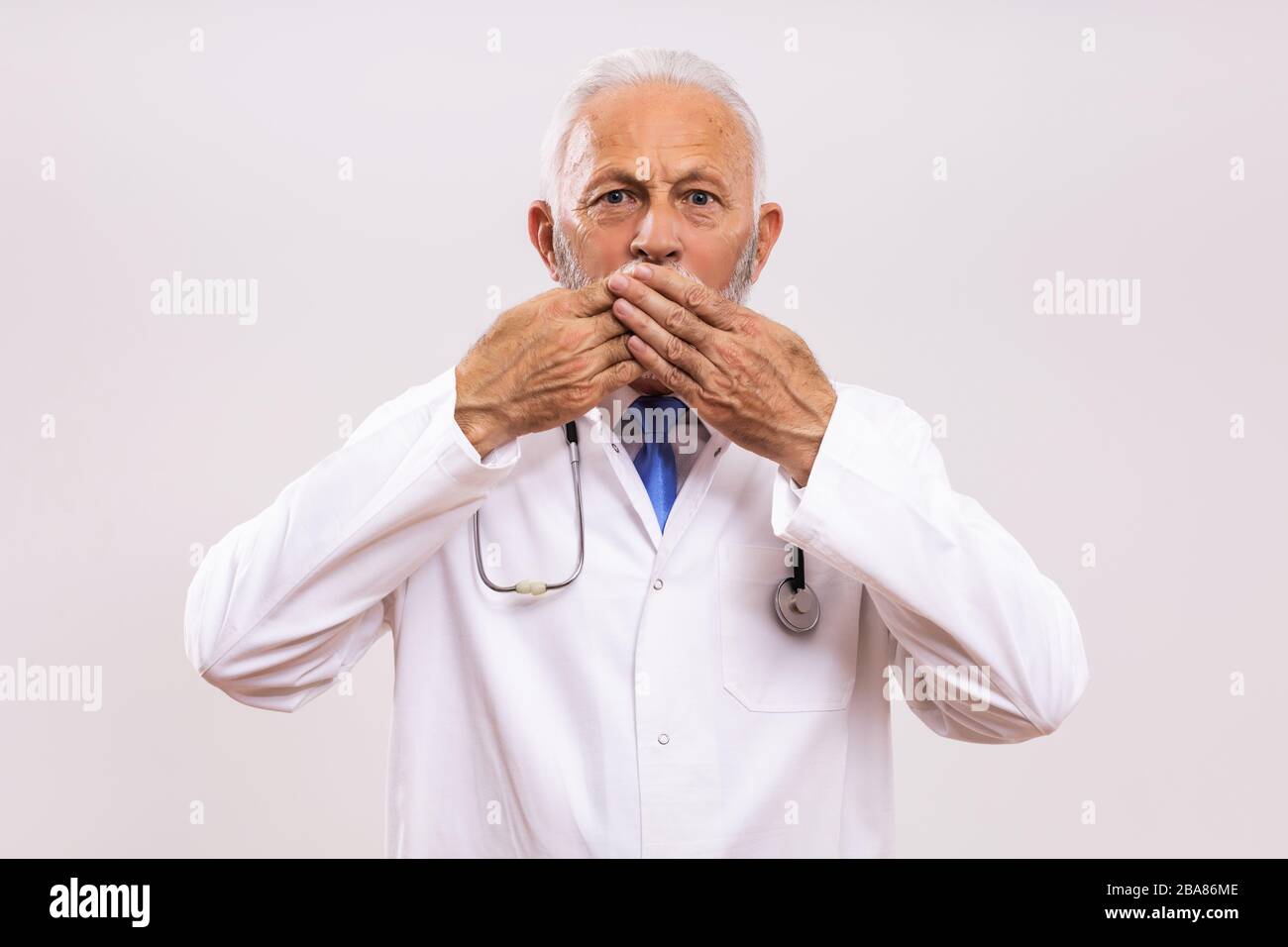 Un médecin expérimenté choqué avec des mains couvrant la bouche sur un fond gris. Banque D'Images