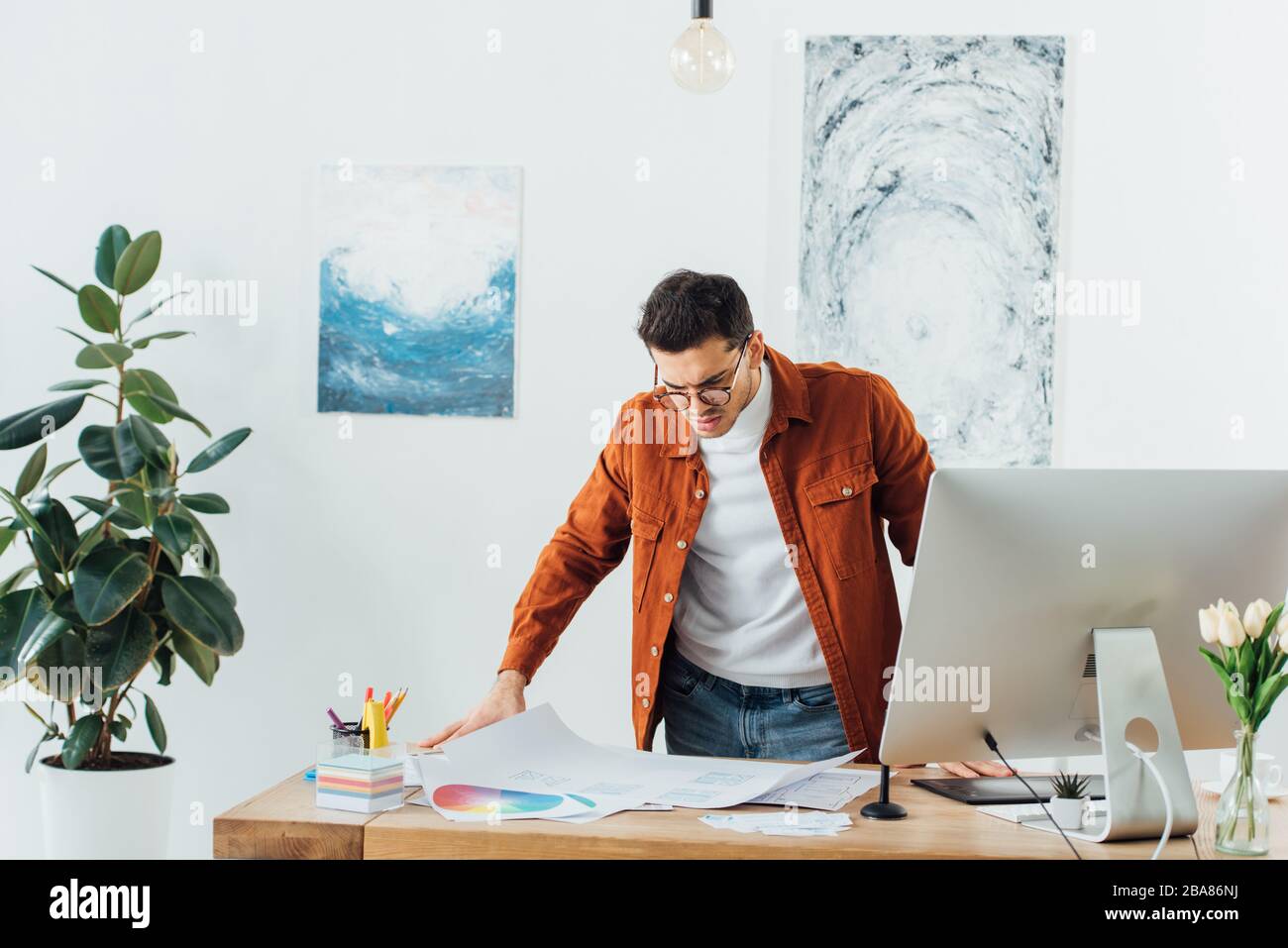 Beau concepteur ux travaillant avec des cercles de couleur et des croquis de site Web près de l'ordinateur sur la table Banque D'Images