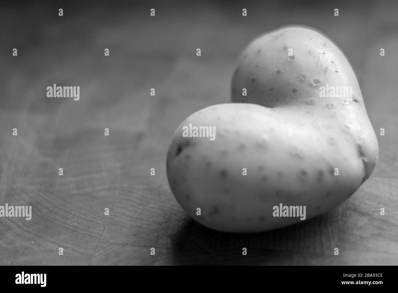 Gros plan isolé d'une pomme de terre brute en forme de coeur unique en noir et blanc Banque D'Images