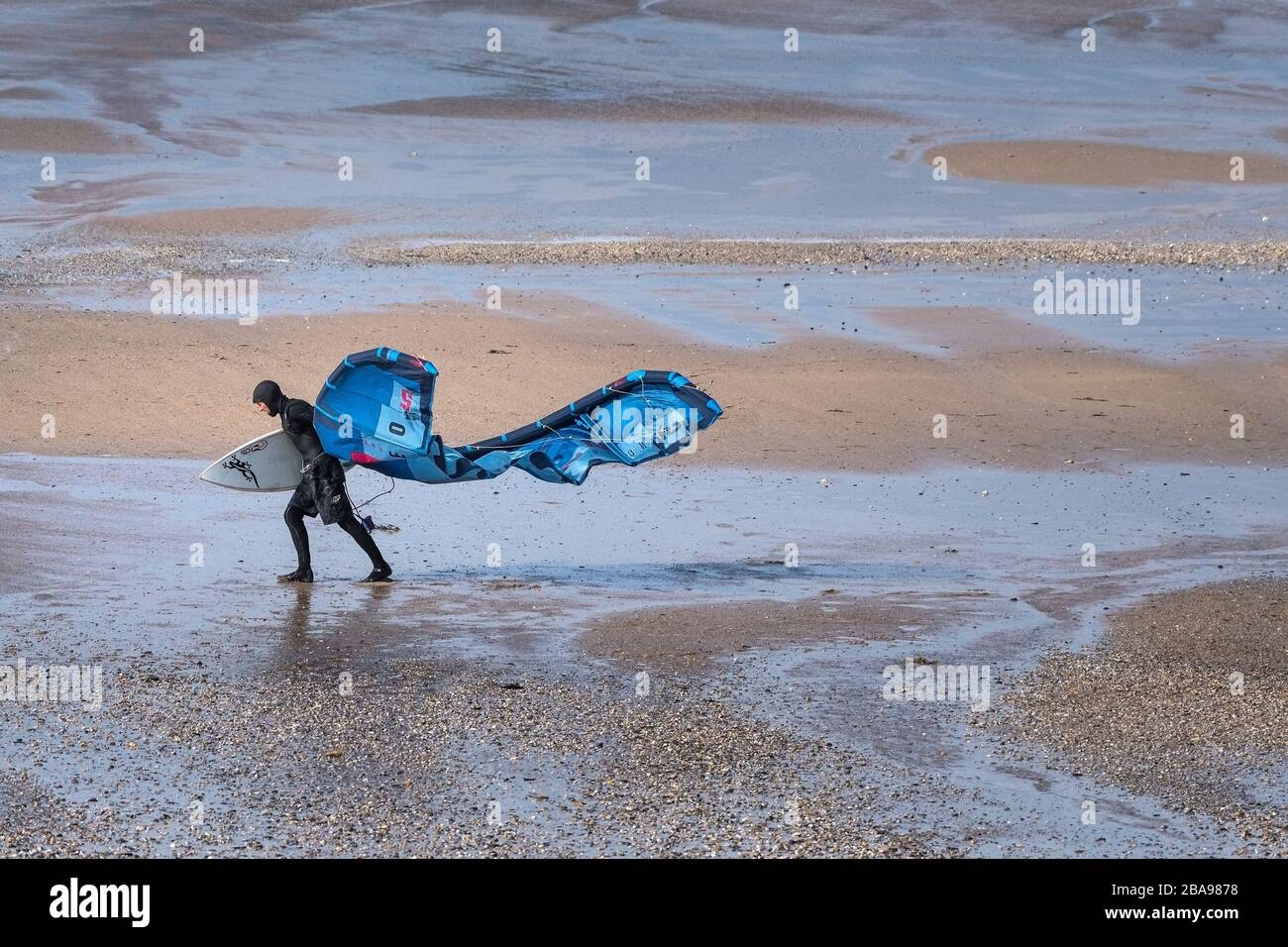 Un surfeur de kite solitaire qui a du mal à transporter son équipement de kite surf en plein vent sur la plage de Fistral à Newquay à Cornwall. Banque D'Images