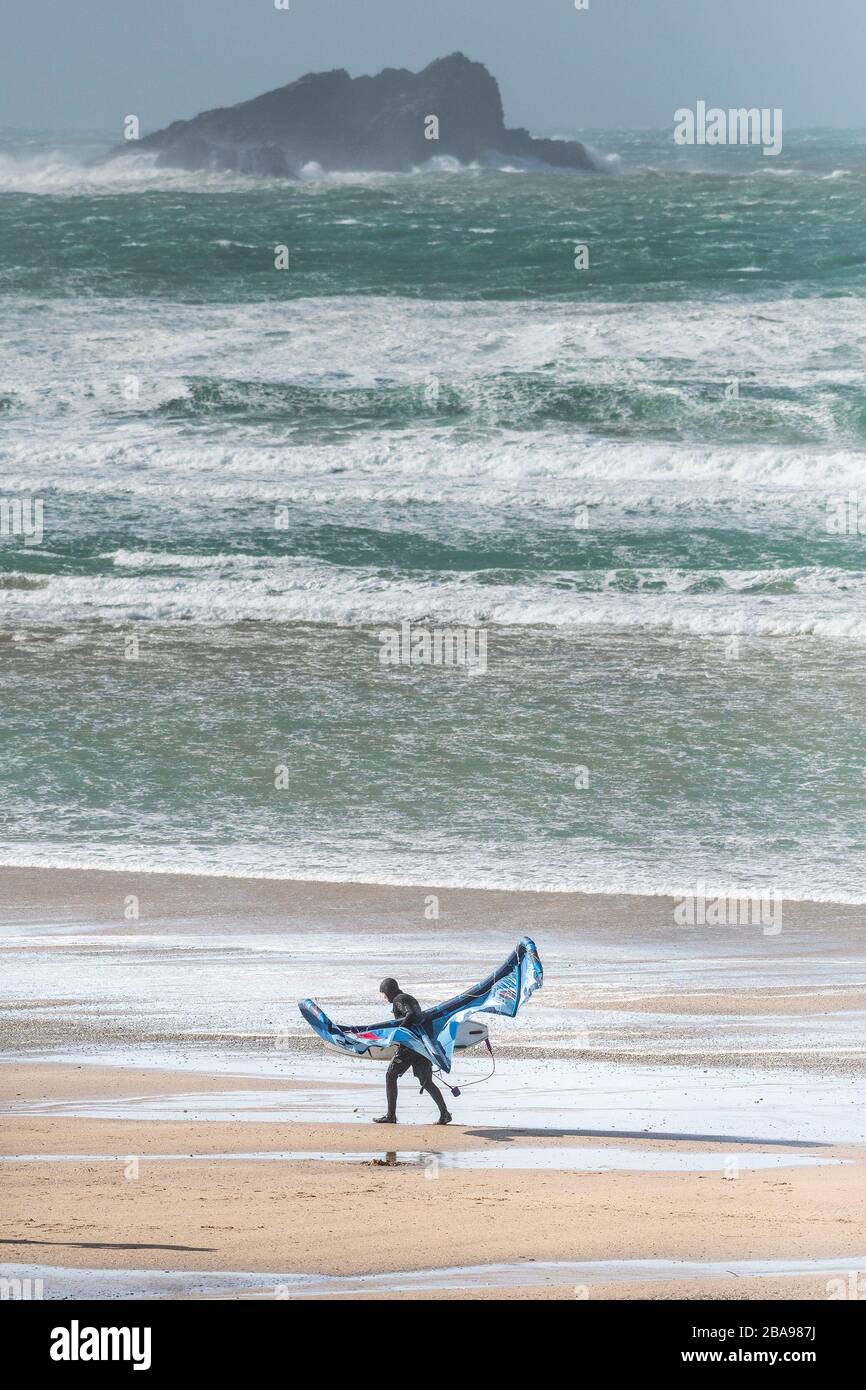Un surfeur de kite solitaire a du mal à transporter son équipement de kite surf dans des vents forts sur la plage de Fistral à Newquay, dans les Cornouailles. Banque D'Images
