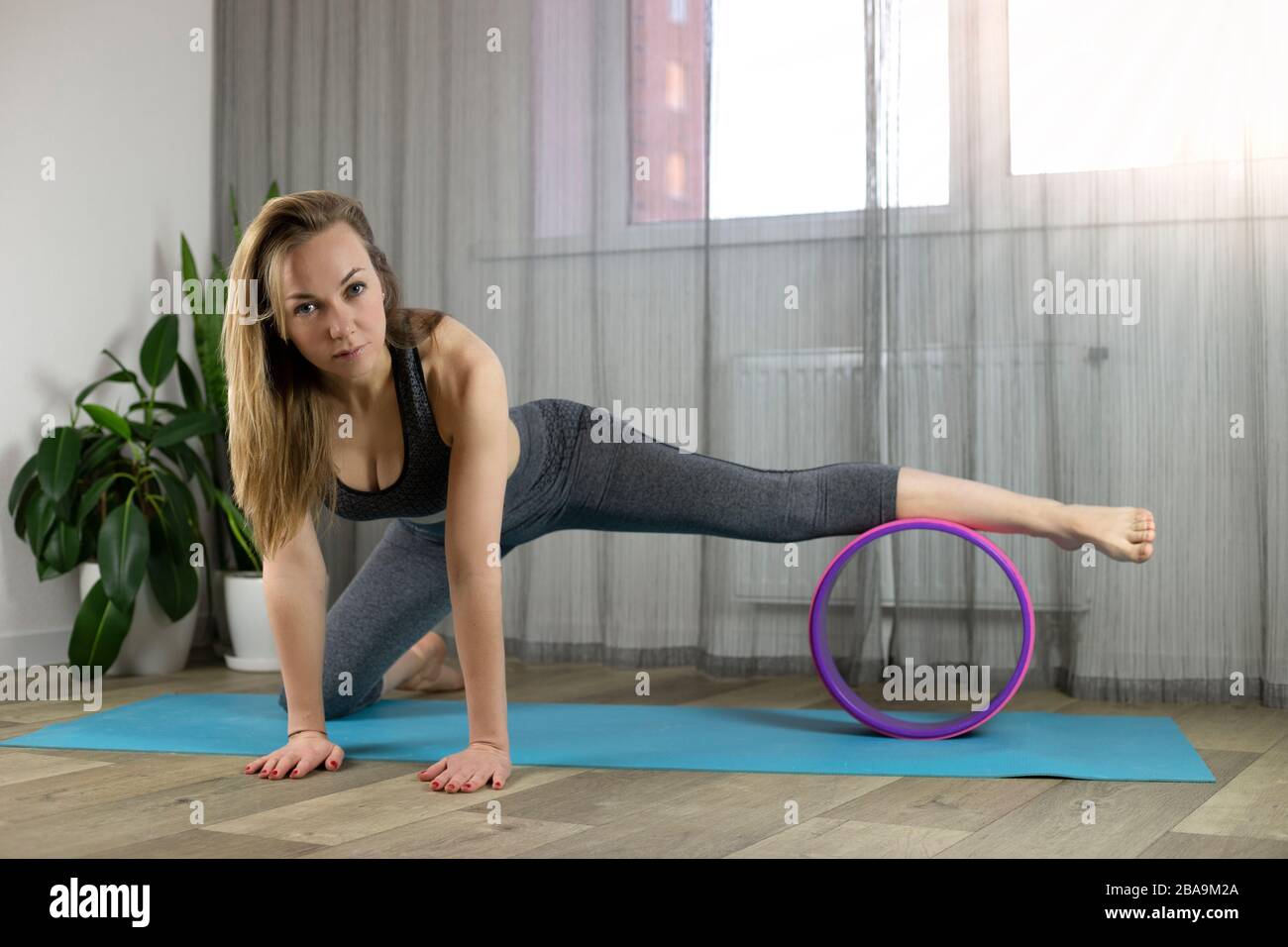 Une petite fille européenne qui fait des exercices d'étirement à la maison sur un tapis de yoga avec une roue de yoga. Rayons de lumière brille de la fenêtre. Torchère. Sport de quarantaine. Banque D'Images