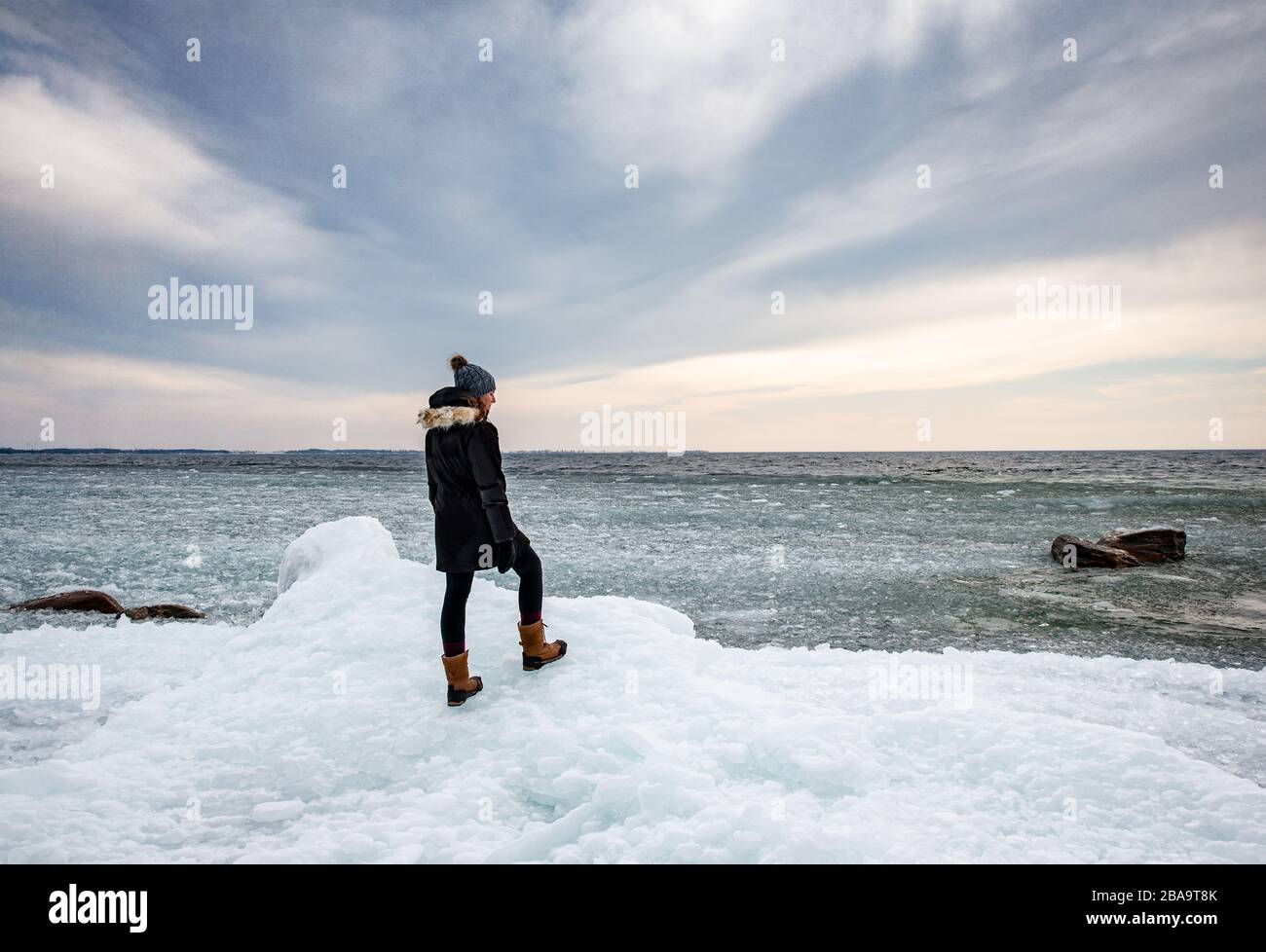 Femme debout sur une rive glacée d'un lac regardant au loin. Banque D'Images