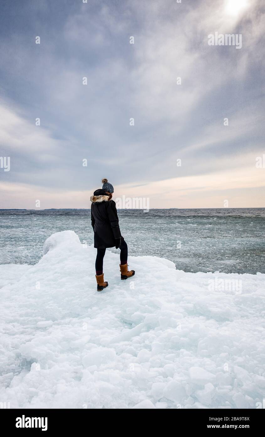 Femme debout sur une rive glacée d'un lac regardant au loin. Banque D'Images