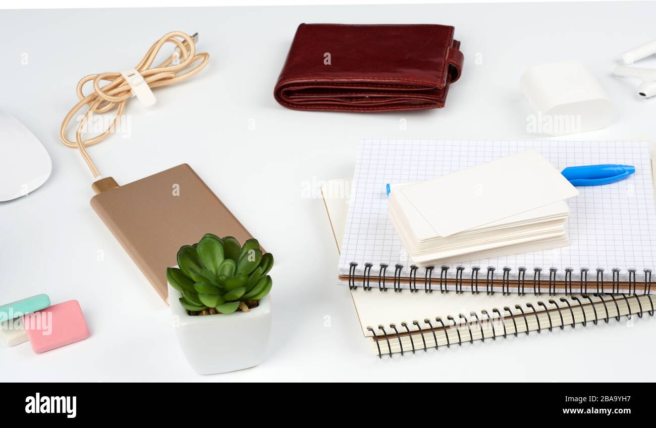 carnets, stylo, pile de cartes de visite, portefeuille en cuir marron et banque d'alimentation avec cordon sur une table blanche, lieu de travail Banque D'Images