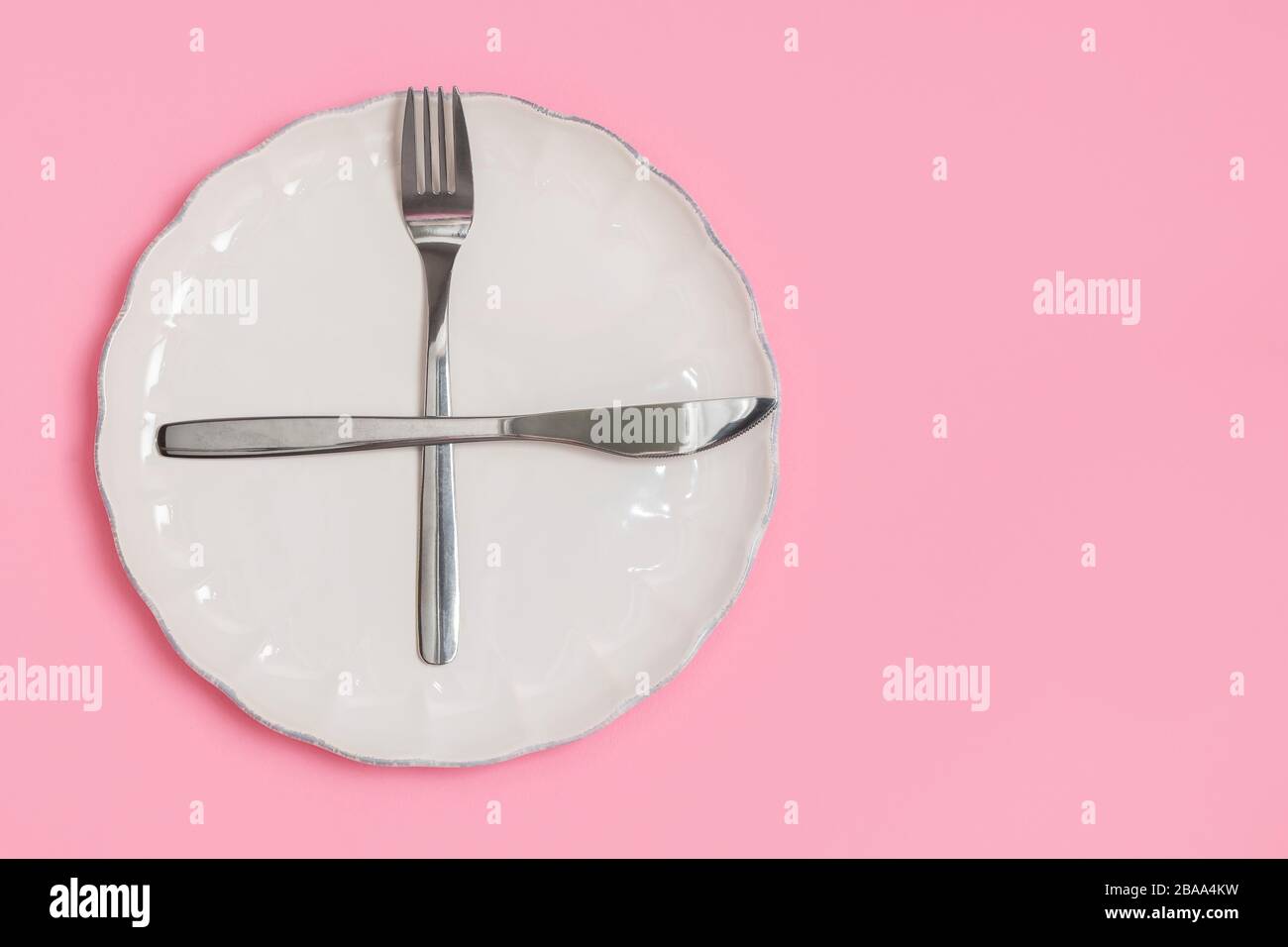 Concept de jeûne intermittent. Directement au-dessus de la vue de la fourche et du couteau sur la plaque blanche sur fond rose. Image avec espace de copie, vue de dessus Banque D'Images