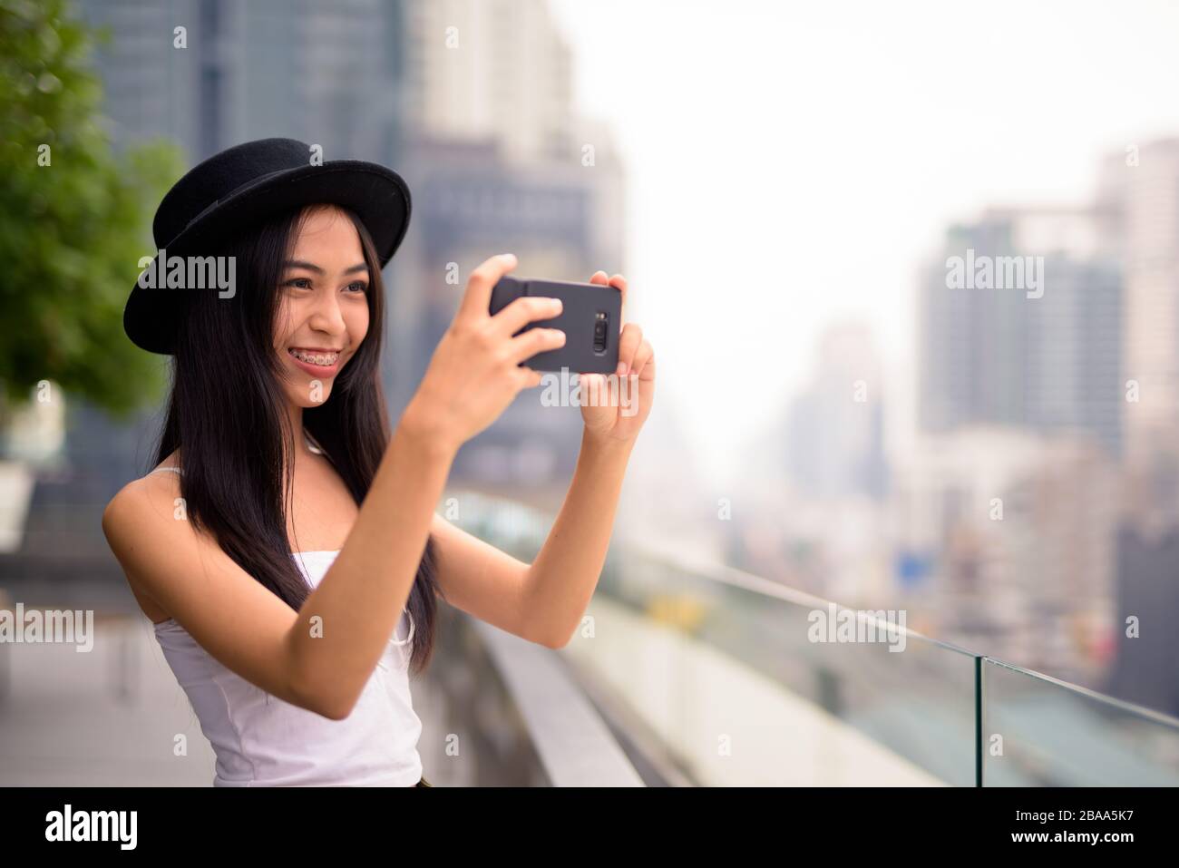 Heureuse jeune femme de tourisme asiatique belle prendre des photos avec le téléphone contre la vue de la ville Banque D'Images