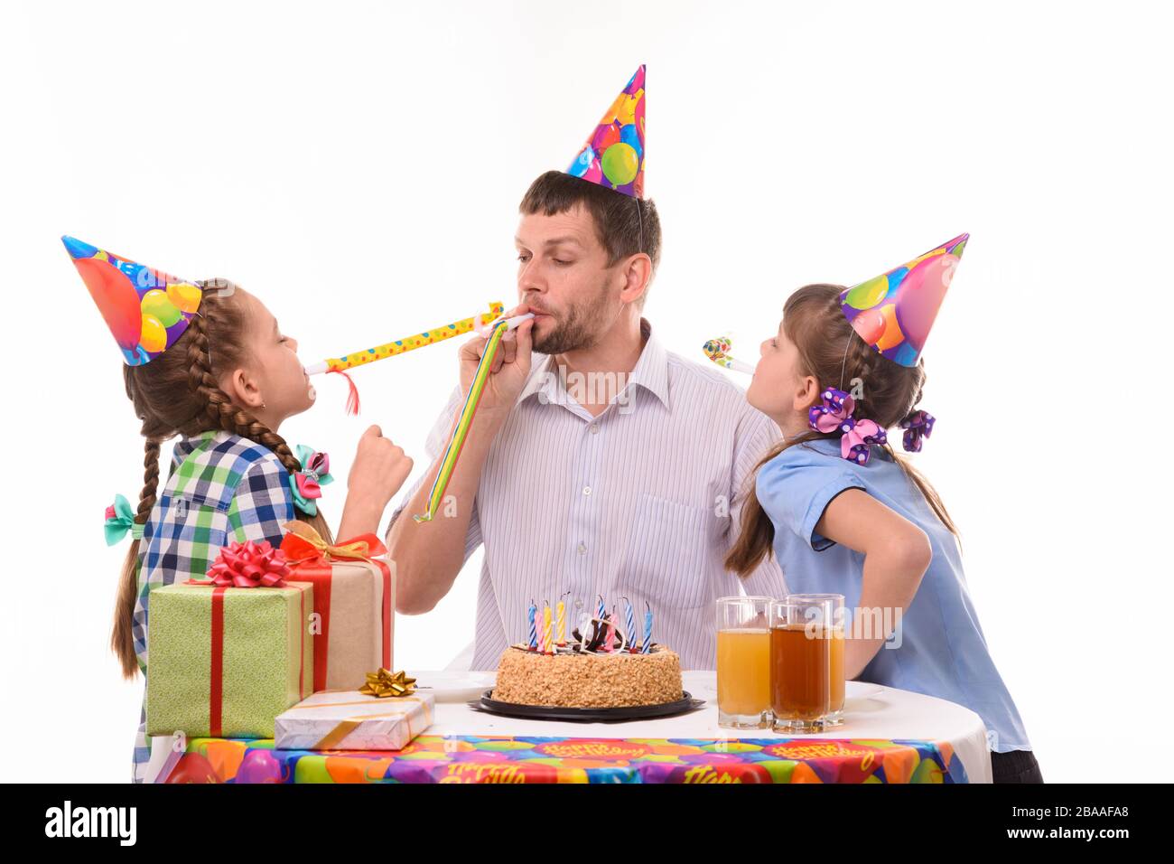 Les enfants et le père soufflent joyeusement les sifflets aux cornes lors d'une fête d'anniversaire Banque D'Images