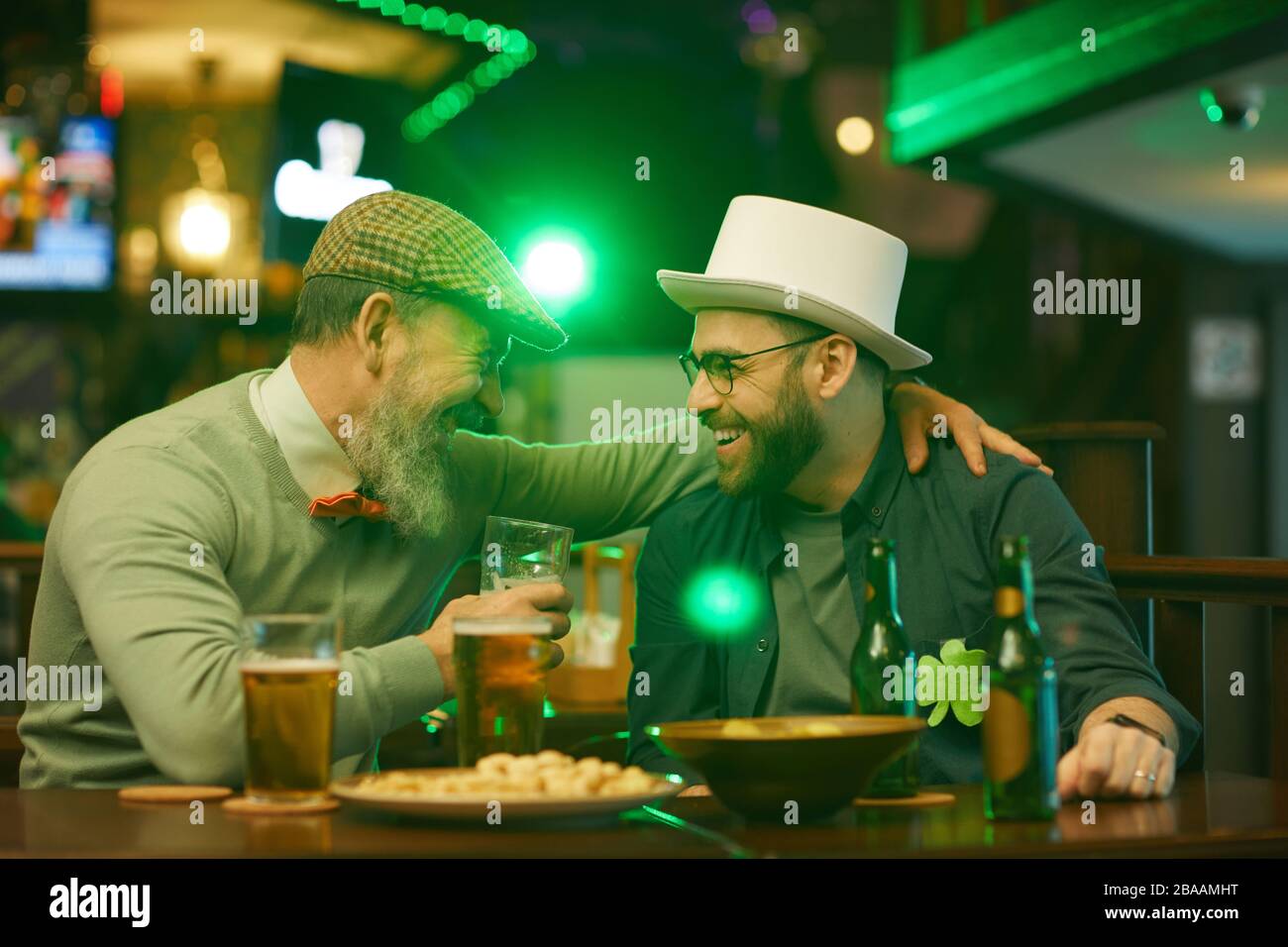 Deux hommes barbus riant et parlant l'un avec l'autre tout en buvant de la bière à la table dans le pub Banque D'Images