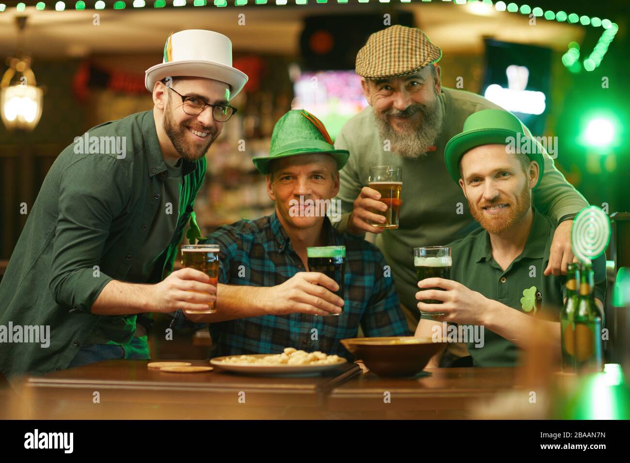 Portrait d'hommes heureux tenant des verres de bière et souriant à l'appareil photo tout en ayant un bon moment dans le pub Banque D'Images