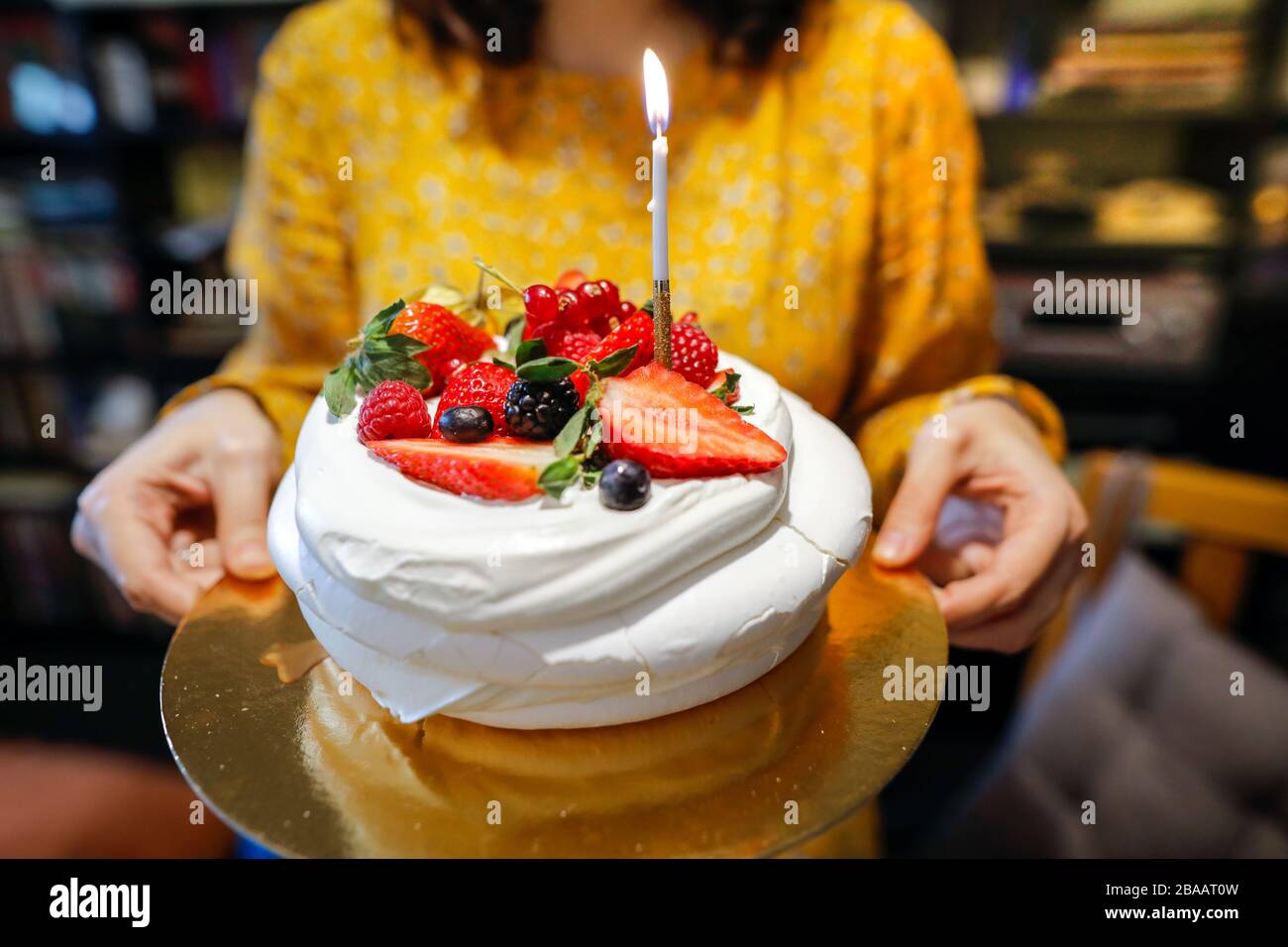 Faible profondeur d'image de champ (foyer sélectif) avec une femme tenant un gâteau meringue de fruits frais avec une bougie éclairée. Banque D'Images