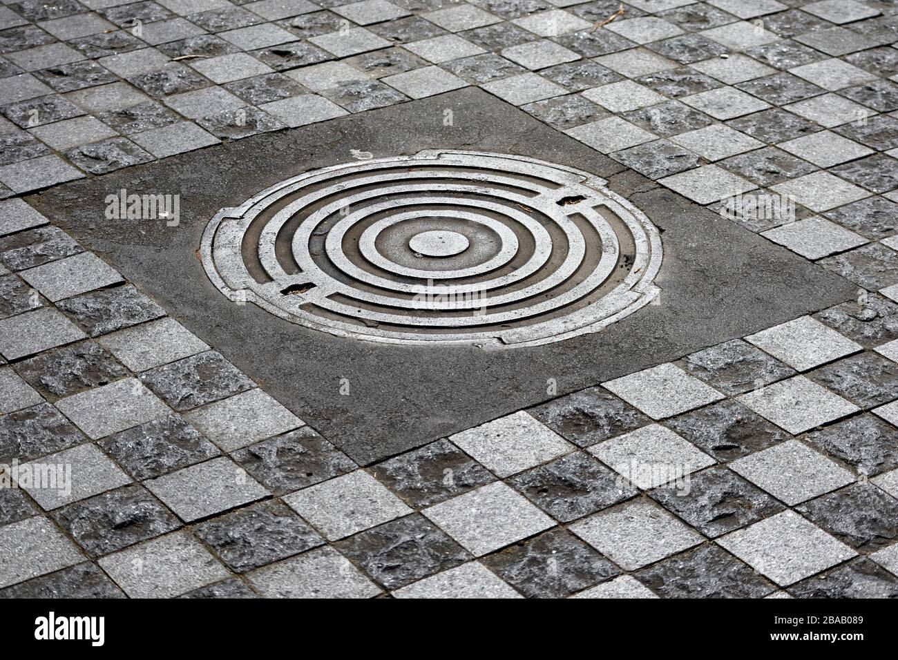 Motifs sur une couverture de trou de Manhole avec des pavés de carreaux entourent à Queen Street, Auckland CBD, Nouvelle-Zélande Banque D'Images