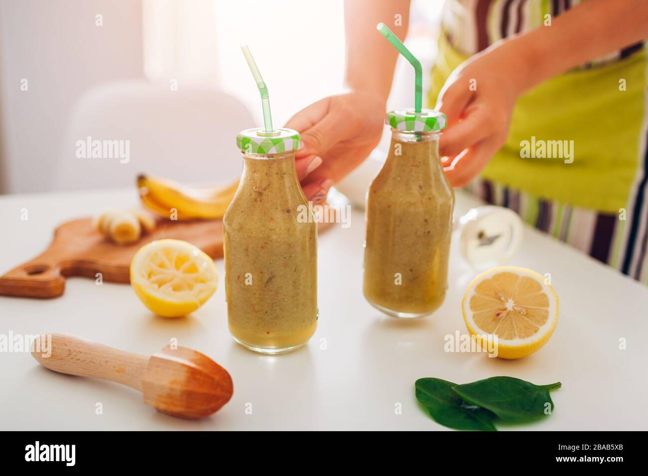 Bouteilles avec épinards et smoothie banane avec ingrédients. Femme met des boissons sur la table de cuisine. Régime sain de detox Banque D'Images