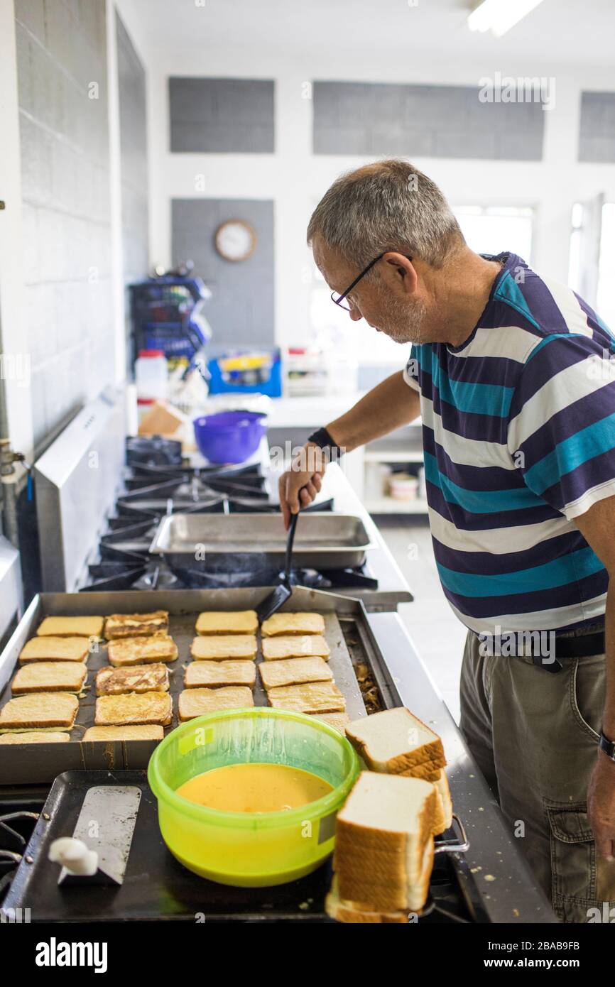 Homme âgé qui cuisine des toasts français dans une cuisine industrielle. Banque D'Images