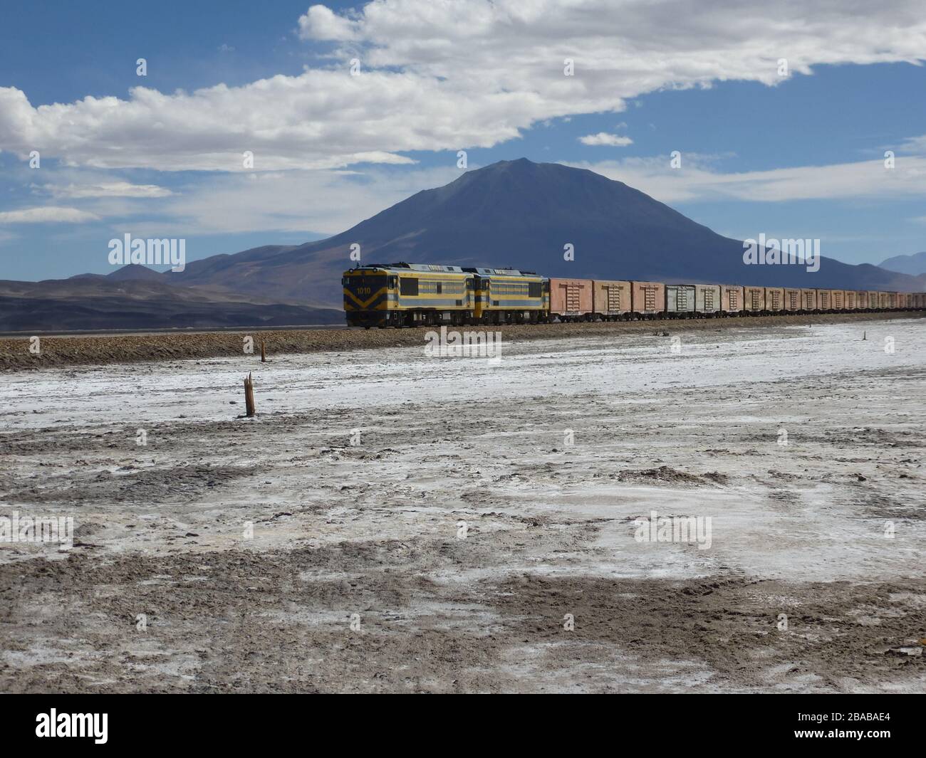 Train long avec de nombreux conteneurs traversant la zone éloignée de bolivie près de salar de uyuni , avec montagne , ciel , sel sol regardant comme neige Banque D'Images